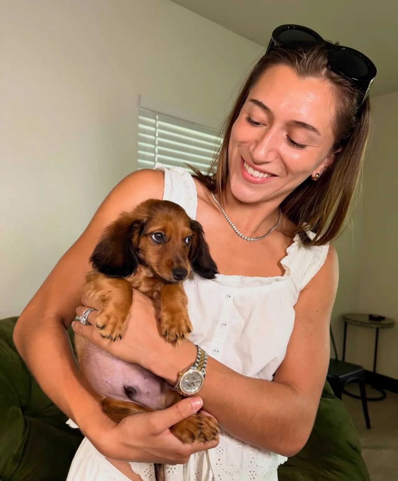 Smiling woman cradling a red long-haired Miniature Dachshund puppy in her arms indoors