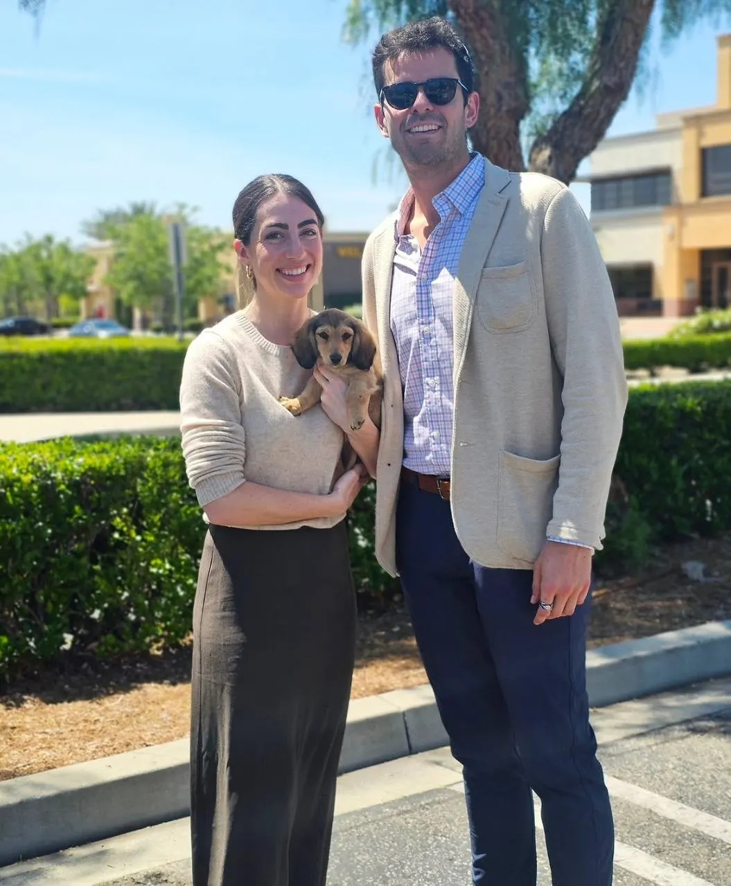Couple standing outdoors holding a cream long-haired Miniature Dachshund puppy on collection day