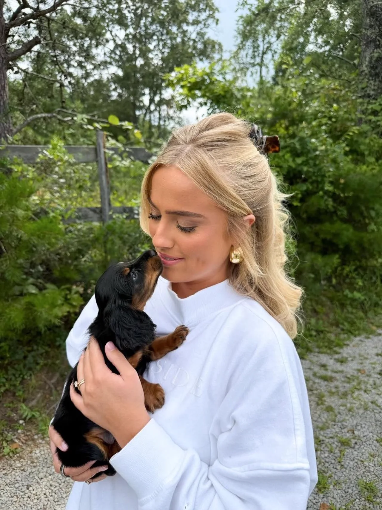 Woman holding a black and tan long-haired Miniature Dachshund puppy that is reaching up to her face