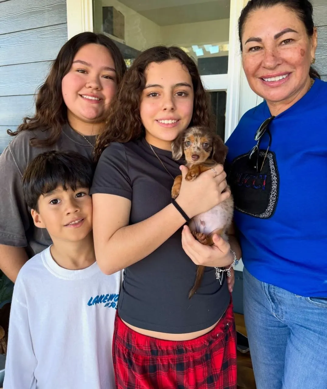 Family gathered on a porch holding a chocolate dapple long-haired Miniature Dachshund puppy