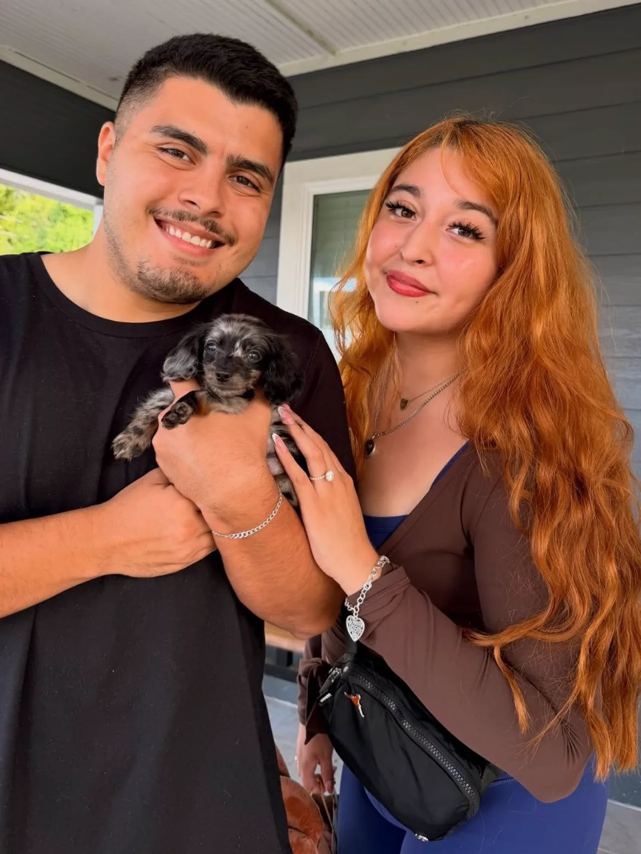 Couple on a porch holding a silver dapple Miniature Dachshund puppy on pickup day